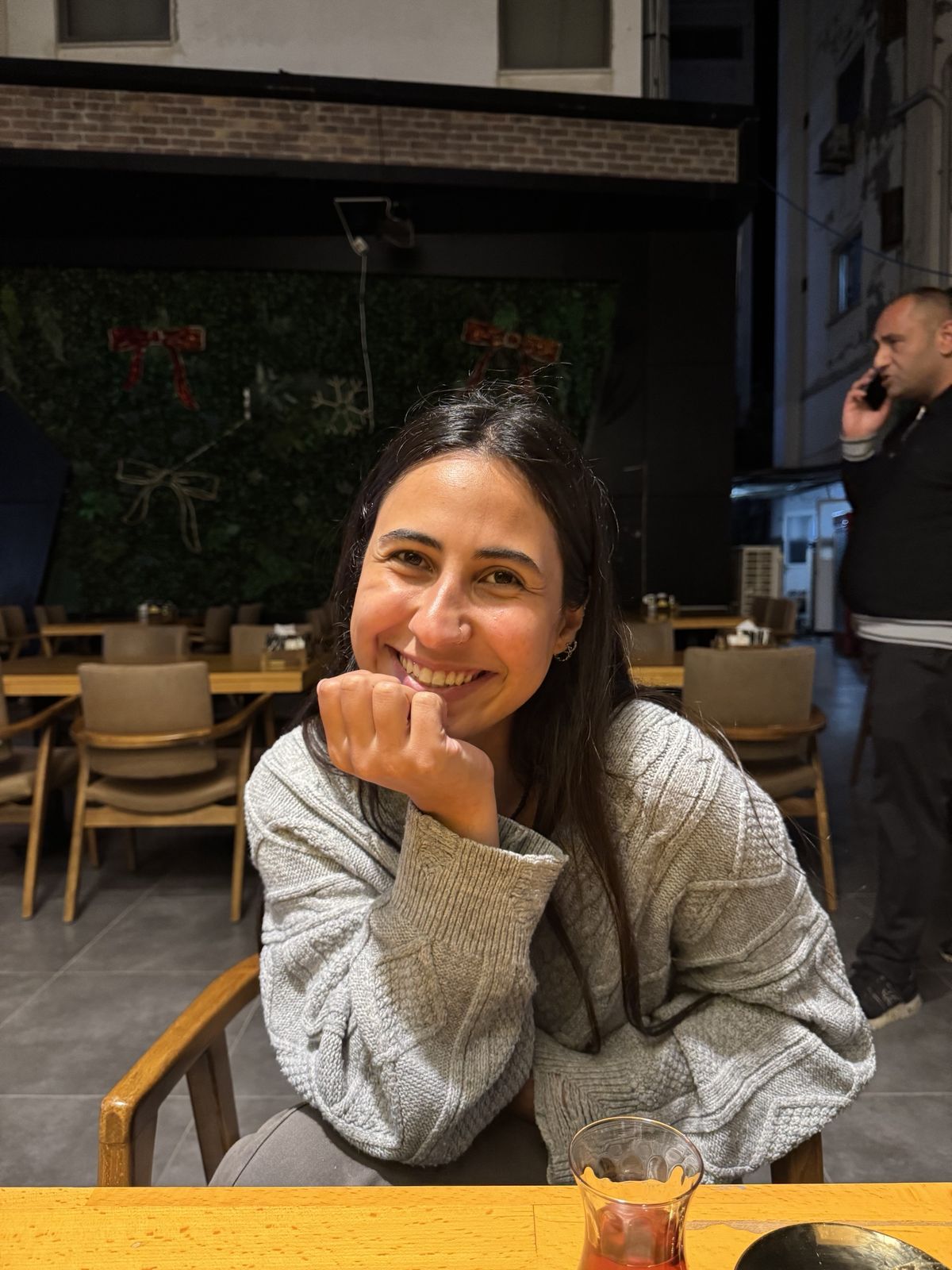 Elif, kafede elini çenesine dayamış gülümsüyor; önünde bir bardak çay